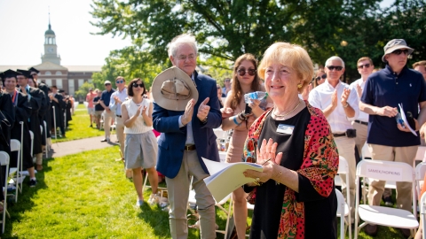 Doris Malesdari S'45 stands and claps and smiles at Commencement, as others in rows behind her also clap and smile.