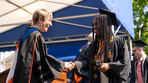 Graduate wearing cap and gown shakes hand with provost