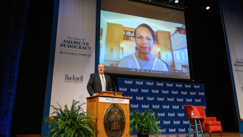 President John Bravman introduces Condoleezza Rice during the Sept. 13 Bucknell Forum event. Bravman stands at a podium with Rice projected on a screen behind him.