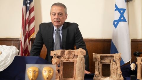 Portrait of Matthew Bogdanos with antiquities from Israel laid out on a table in front of him.