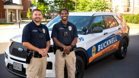 Two Bucknell Public Safety officers pose next to a Public Safety vehicle.