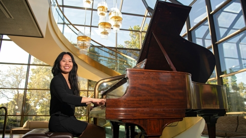 Vivian Kuang sits at a grand piano in a black suit.