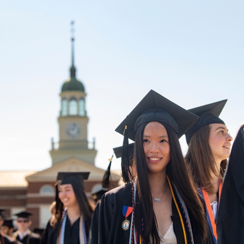 A student walks in front of Bertrand library with her peers on graduation day.