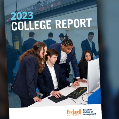 The cover of the Freeman College of Management&#039;s 2023 Annual Report, which features an image of four students looking at a computer in the Moriarty Investment Lab in Holmes Hall