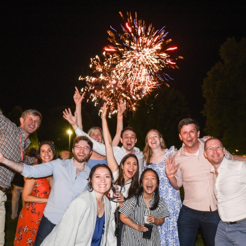 Alumni pose for a photo in front of fireworks