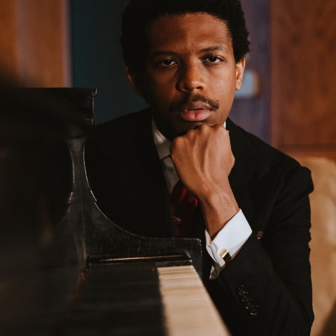 Sean Mason rests his head on his fist as he looks out at one end of the piano keyboard