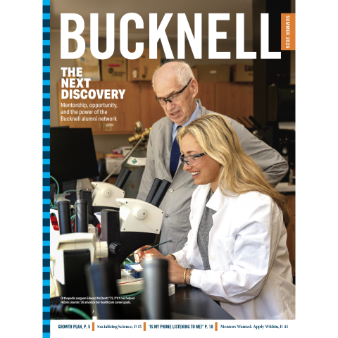 A student in a white lab coat and a man in a gray coat peer into a microscope