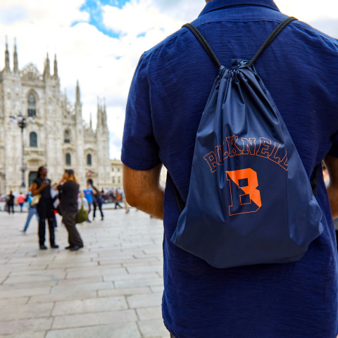 Bucknell student in a square in Milan. Student is facing away from the camera, wearing a Bucknell backpack. Cathedral in background. 