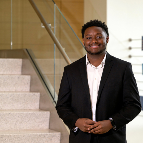 Jerimaha McClain wears a dark suit and white dress shirt and stands at the base of a stairway in Holmes Hall.