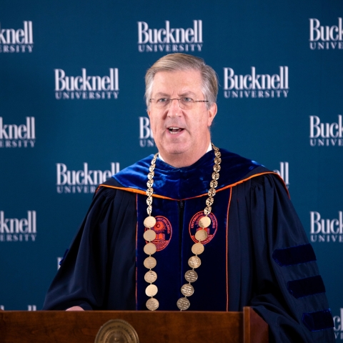 President John Bravman speaks at podium dressed in regalia