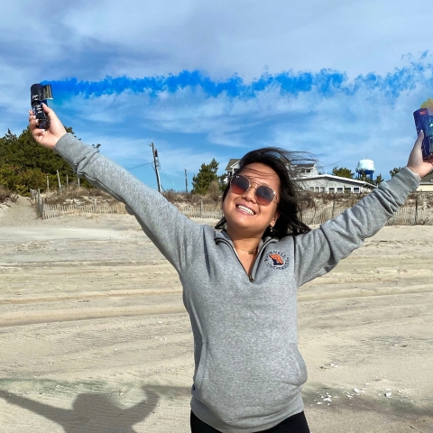 Katie Shives '24 holds orange and blue smoke bombs.