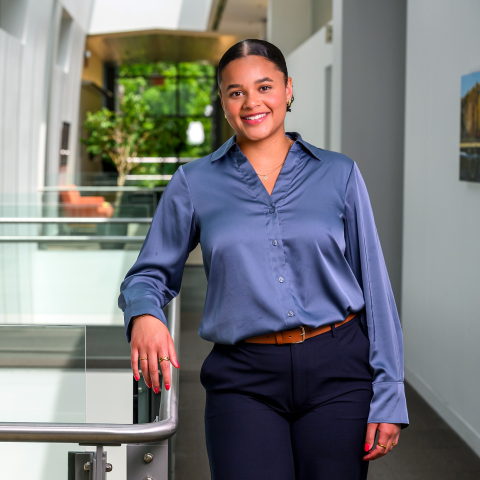 Haden Williams wears a blue shirt and smiles while leaning against a railing in a modern office setting.