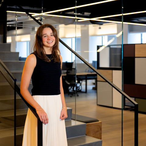Kelly Byrne stands at the bottom of a staircase with an office scene in the background.