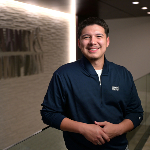 Vincent Torres stands and smiles with a Kearney & Company logo on a wall behind him.