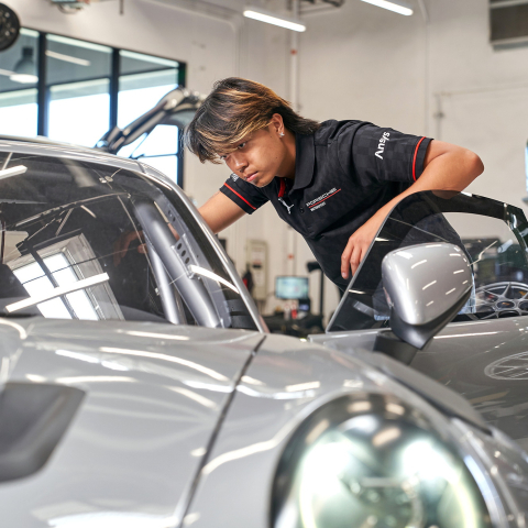 Zach Ebilane is standing and looking into the driver's side of a silver Porsche.