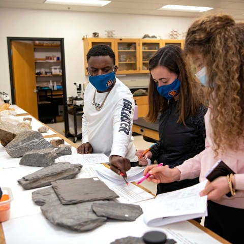 Students wearing masks look at rocks in a geology class