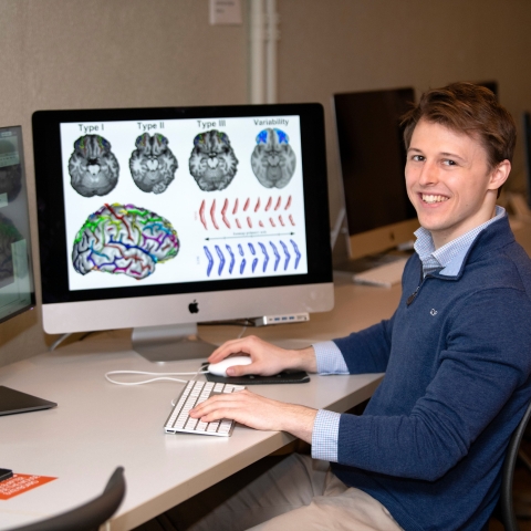 Will Snyder '21 sits at desk with computers displaying brain scans