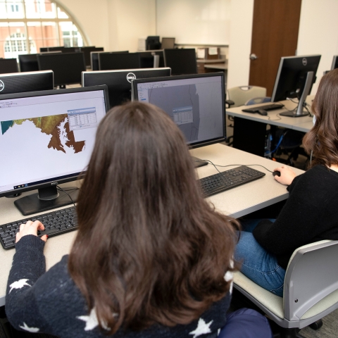 Two students sit and look at maps on their computer