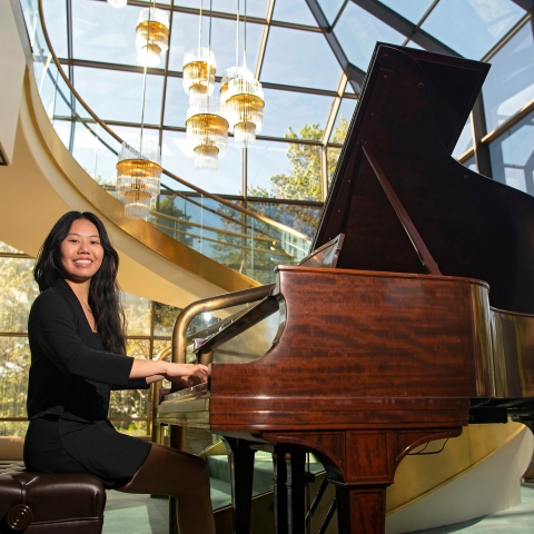 Vivian Kuang sits at a grand piano in a black suit.