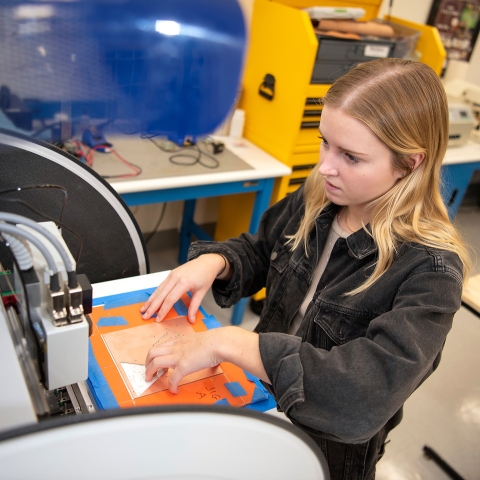 Student creating a circuit board with machinery