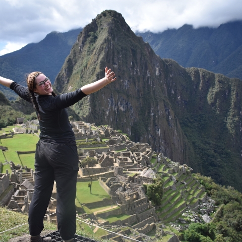 Student standing above Machu Picchu with arms outstretched
