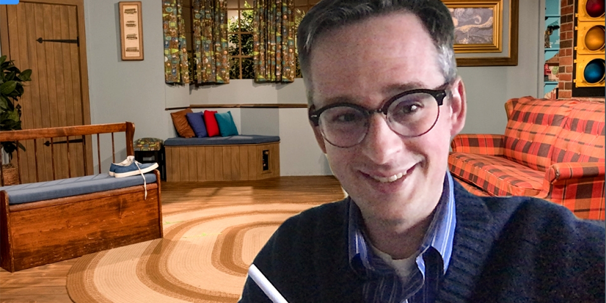Evan Peck in a Zoom meeting with the Mr. Rogers&#039; Neighborhood home background behind him.