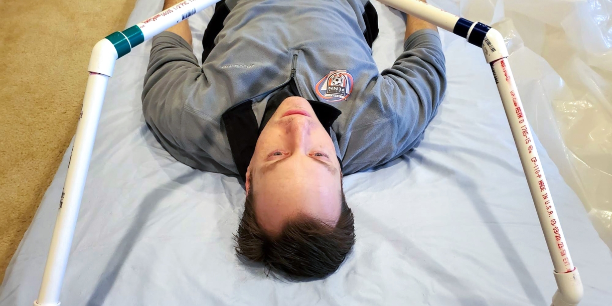 Professor Brandon Vogel lies under the frame of a prototype intubation tent.
