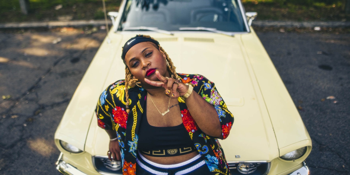 Oompa Williams &#039;14 leans on the hood of a yellow mustang showing a peace sign.