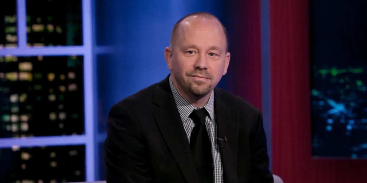 professor Jon A. Shields sits in a chair, dressed in a black suit