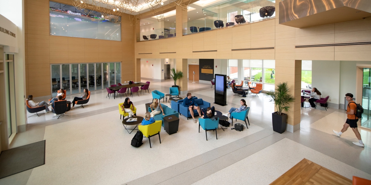 A down angle photograph of students walking and sitting in the lobby of Holmes Hall.