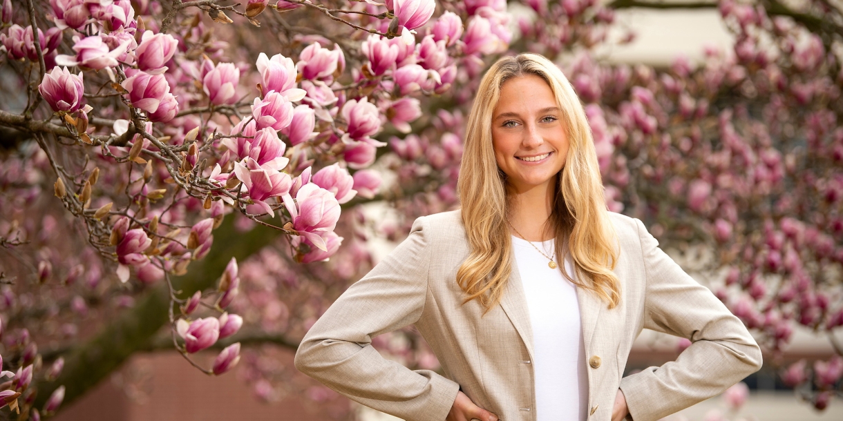 Abigail Kates &#039;24 stands with her hands on her hips and smiles, cherry blossoms are in the background