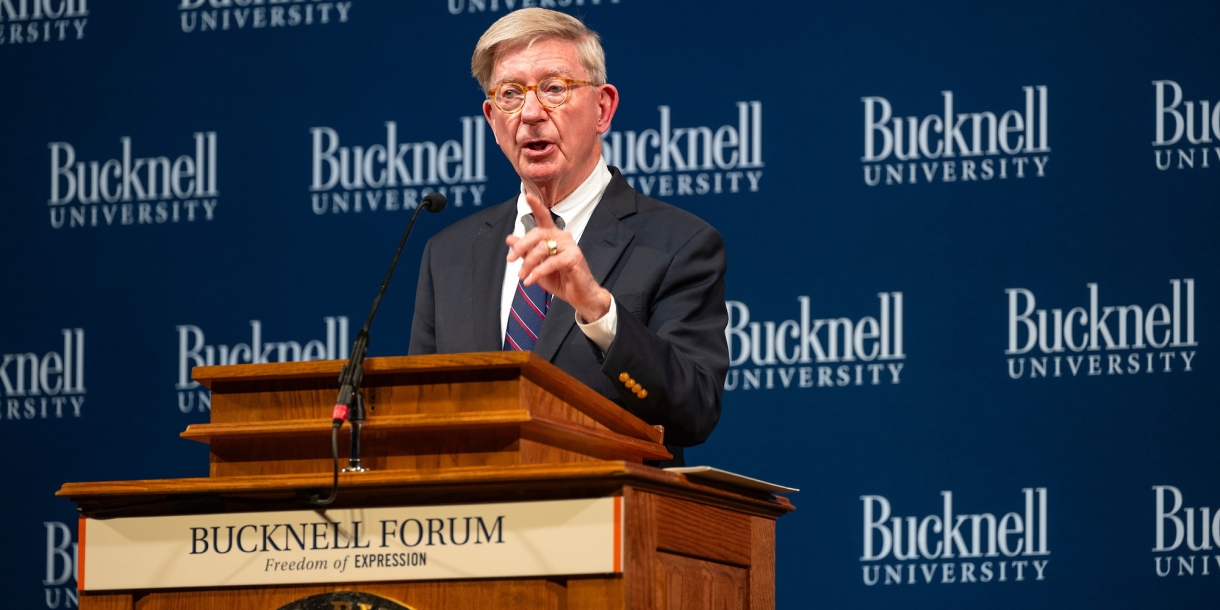 George Will speaks from a podium with a &quot;Bucknell Forum&quot; plaque.