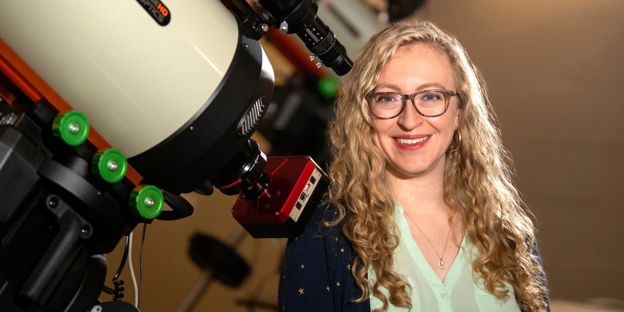 Professor Jackie Villadsen stands next to a large telescope on Bucknell's campus and smiles.
