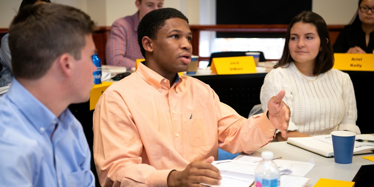 A student asks a question in a management class as two other students look on