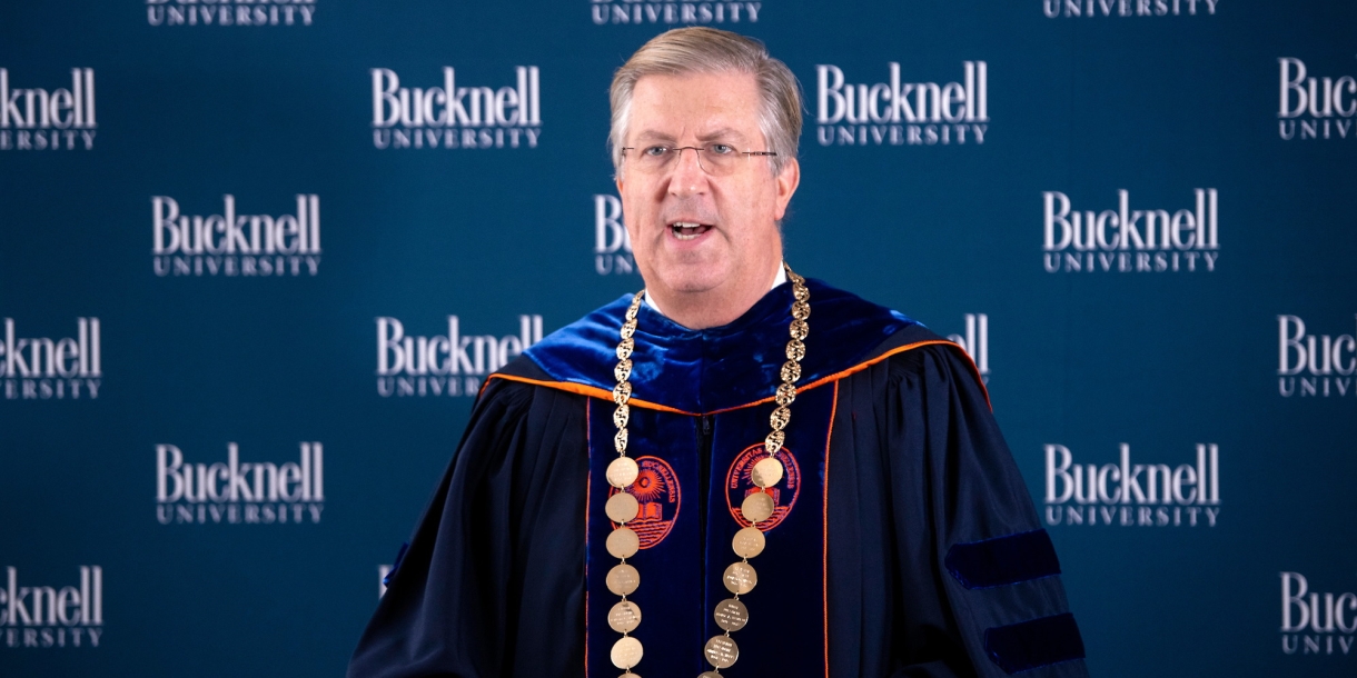 President John Bravman speaks at podium dressed in regalia