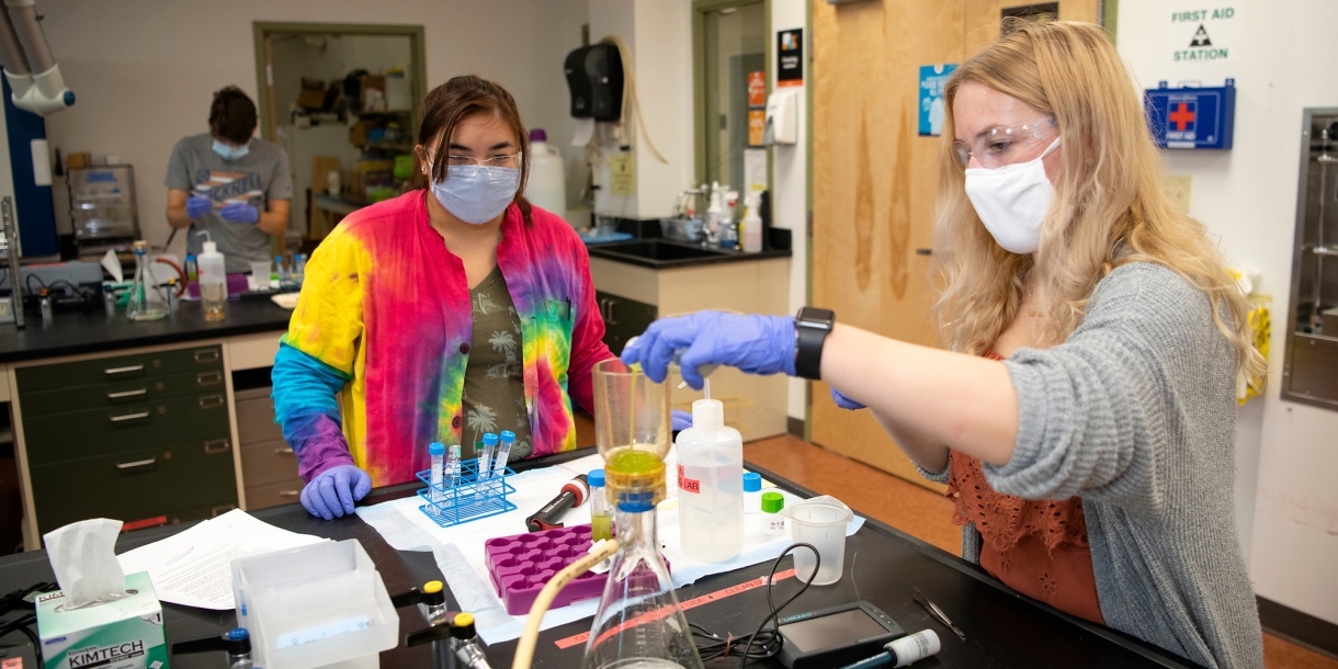 Jackie Zak pumps liquid into a vial with a pipette as Leah Henk watches