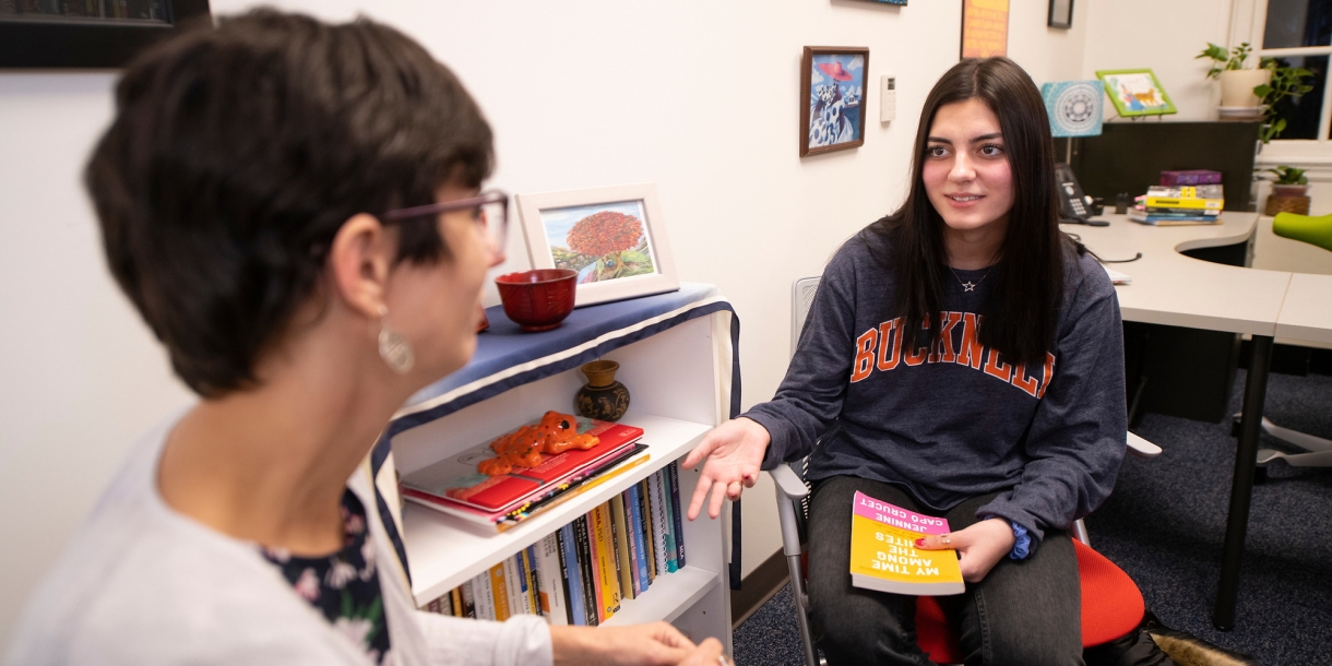 Professor Elena Machado and Emily Sanchez &#039;23 talk in a faculty office, Sanchez holding a book