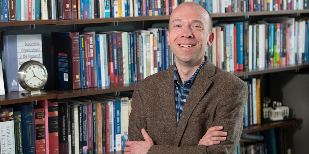 Scott Meinke poses for portrait in front of bookshelf