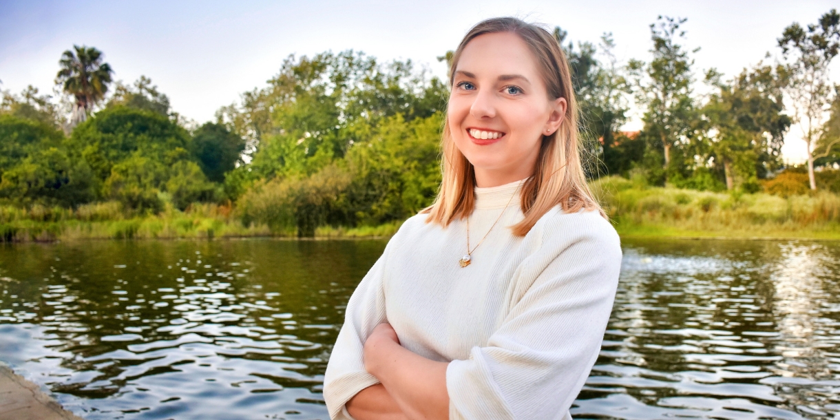 Christina Sfedu &#039;12 stands with her arms crossed in front of a lake.