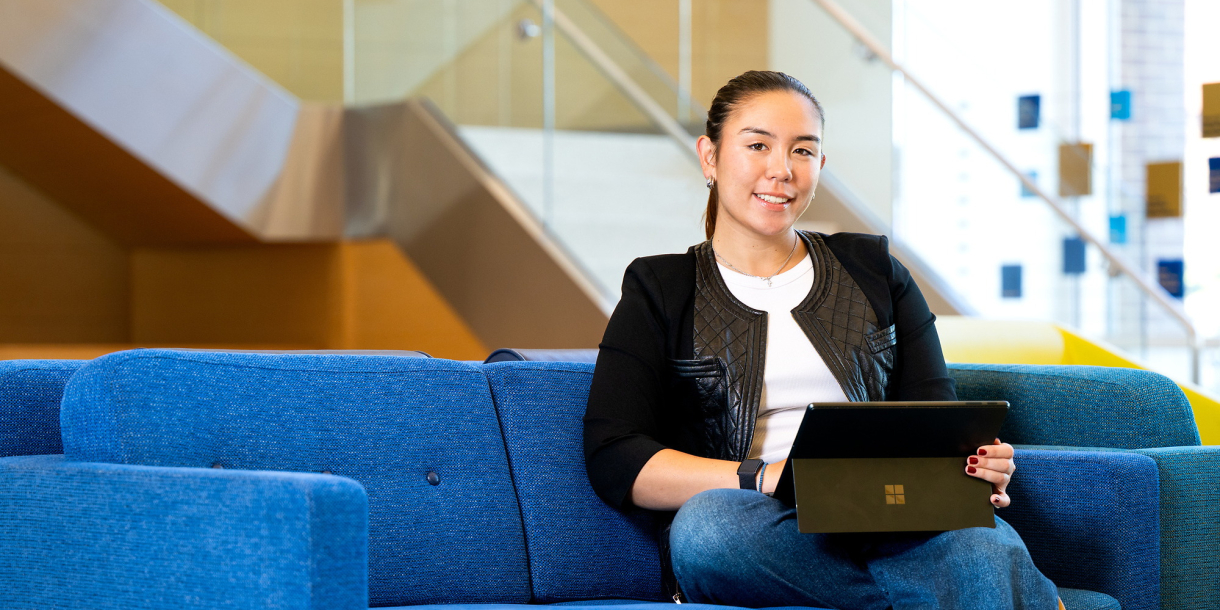 Sophia Bardunias sits on a blue couch in Holmes Hall with a laptop on her lap.