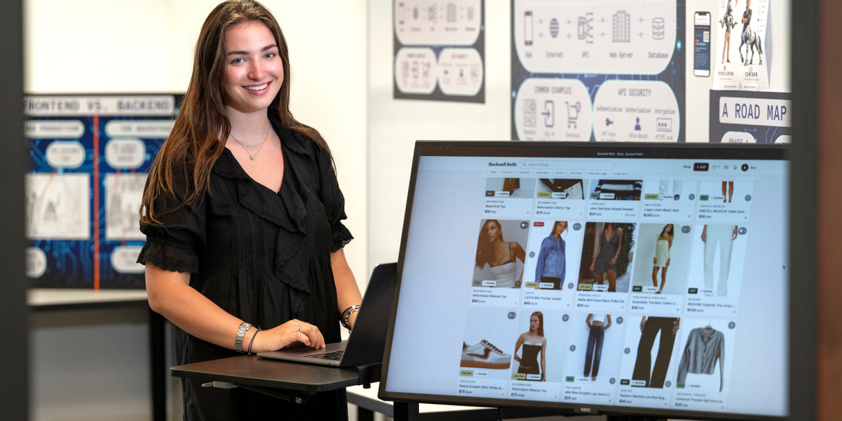 Ava Sklar smiles beside a monitor displaying clothing listings on her Bucknell Refit website.