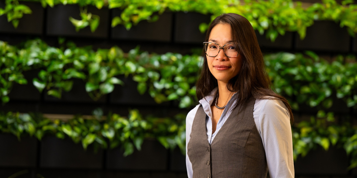 Christine Ngo stands in front of a green, leafy background.