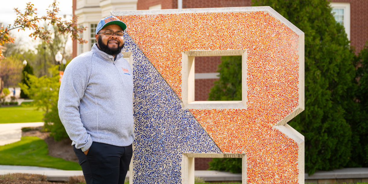 Jawaad "KJ" Benson stands next to a large letter B that is part blue and part orange.