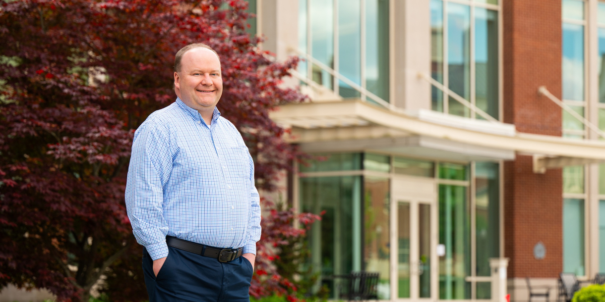Joe Wilck stands with his hands in his pockets and smiles outside of Holmes Hall.