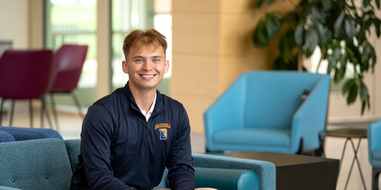 Kaleb Eger sits on a teal chair and smiles.
