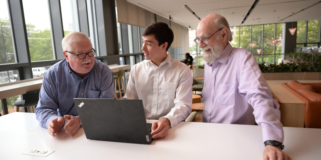Max Quan is working on a laptop in an office setting with David Hamill to his right and Jack Hoadley to his left.