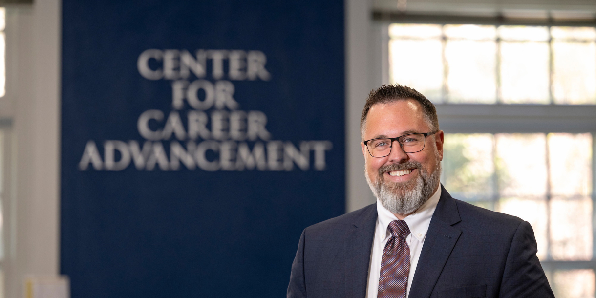 Sean Schofield poses in a suit before a sign that says "Center for Career Advancement"