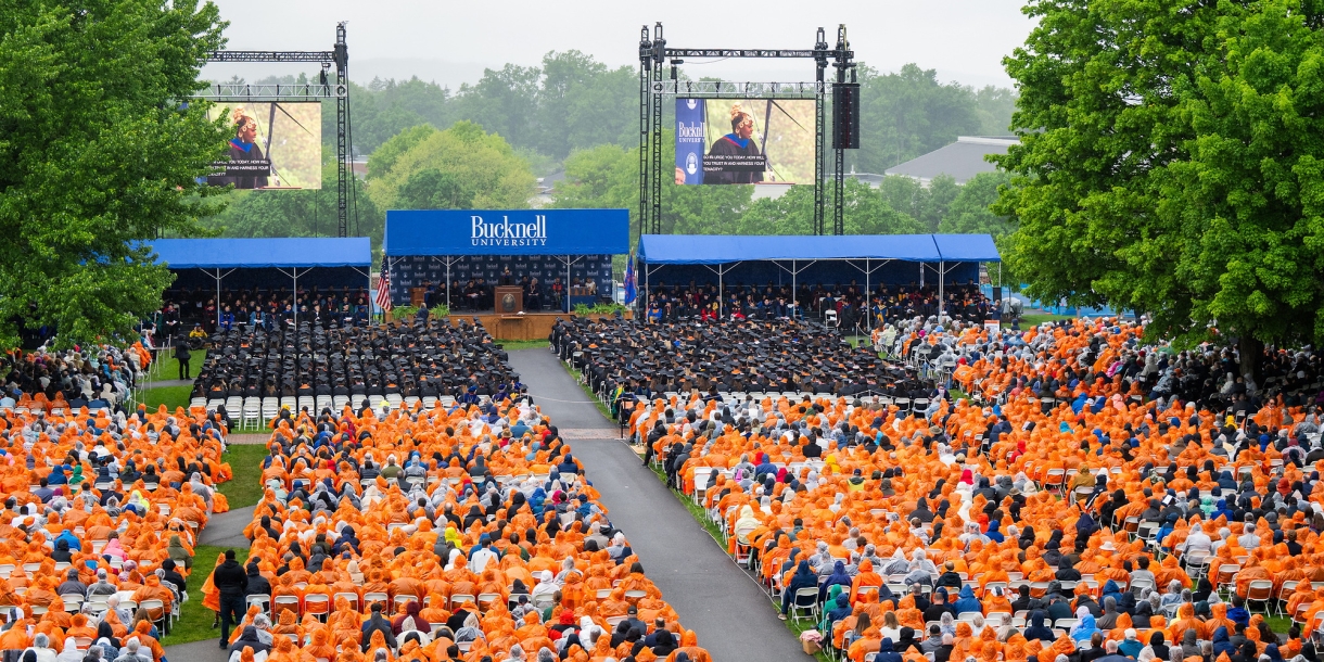 Rows of seniors sit facing the Commencement platform, many dressed in orange ponchos due to rain, at the 2024 Commencement.