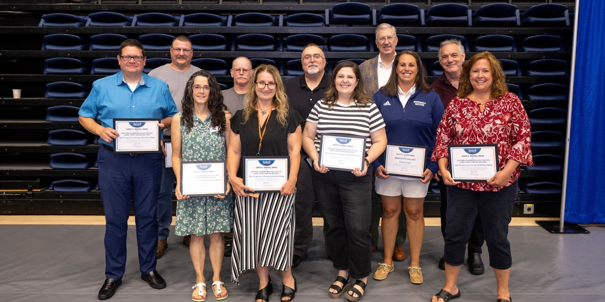 10 employees stand with John Bravman and smile while holding awards