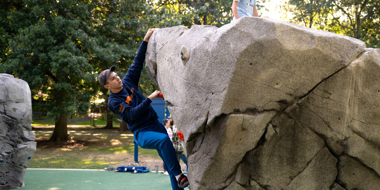A student in a blue shirt climbs on a boulder in Bucknell's bouldering park.